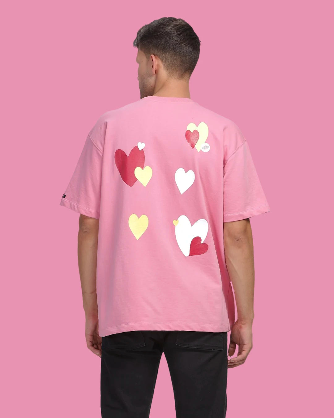 Person wearing a pink t-shirt with heart designs on the back against a pink background