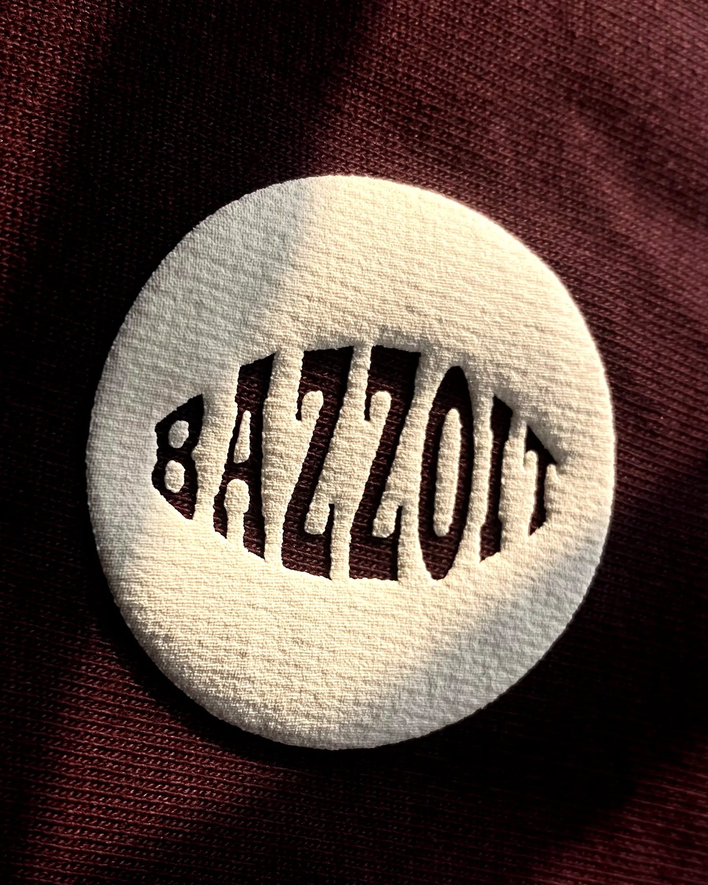 Round white object with 'BAZZOIT' text on a dark background