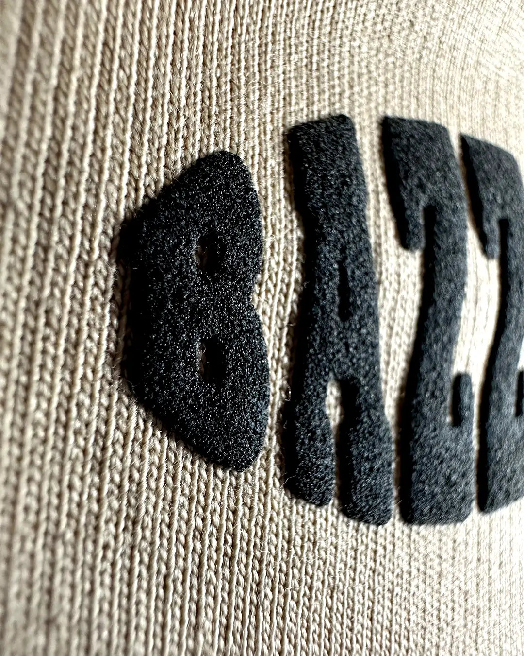 Black letters spelling 'BHAZZOIT' on a beige T SHIRT background