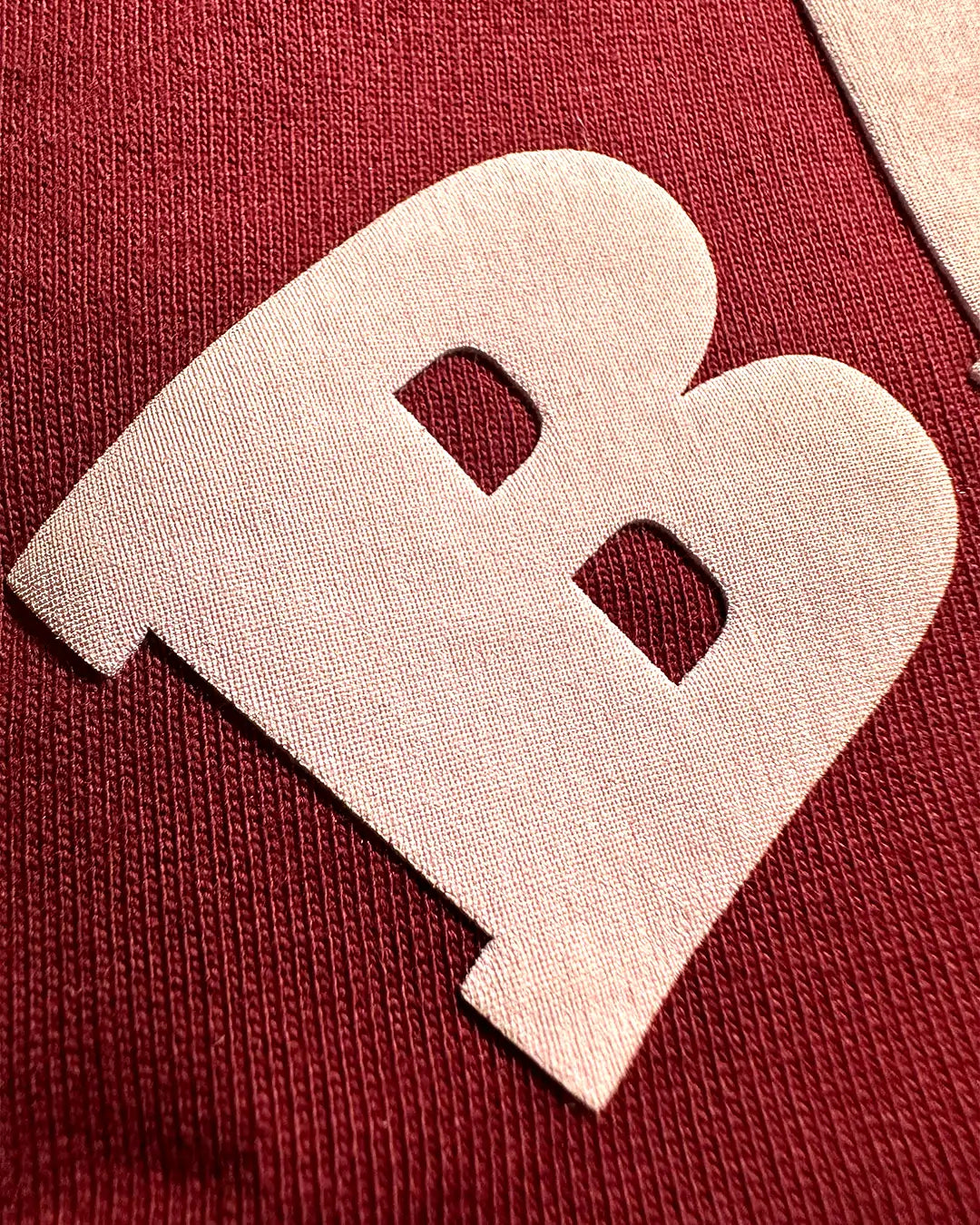 Baby pink heart-shaped object with cut-out design on a Maroon fabric background