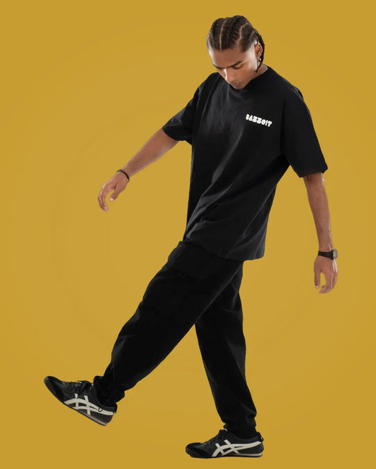 Person wearing a black t-shirt with text and black pants on a mustard yellow background